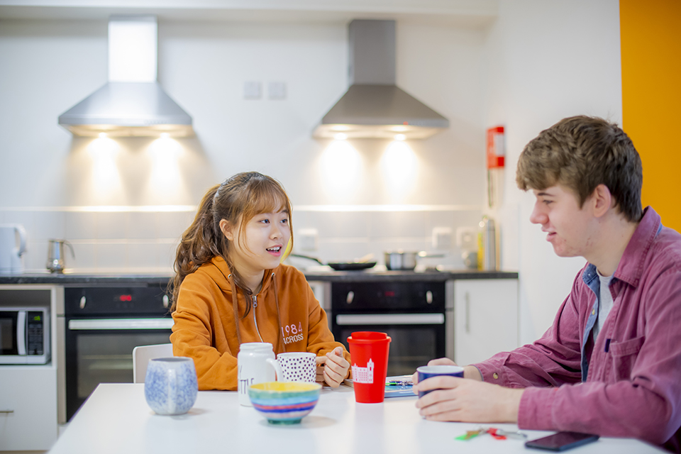 Two students smiling and chatting in the shared, clean, white kitchen.